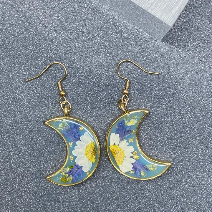 Crescent moon-shaped earrings with floral design on a gray textured surface