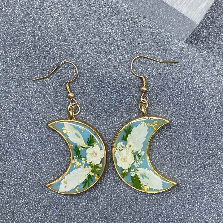 Floral crescent moon earrings on a textured gray surface