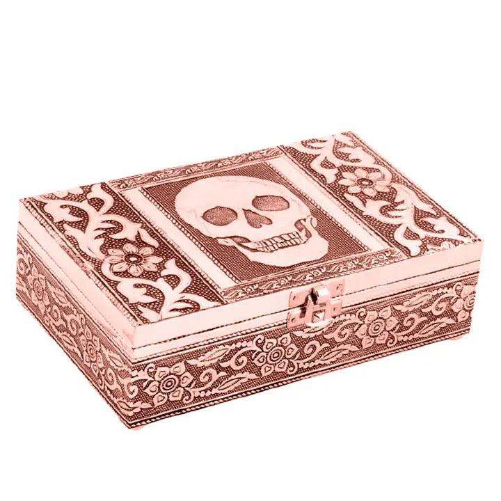 A rectangular decorative box with a skull motif on the lid, featuring ornate floral scrollwork patterns in a metallic rose gold finish, set against a plain white background.