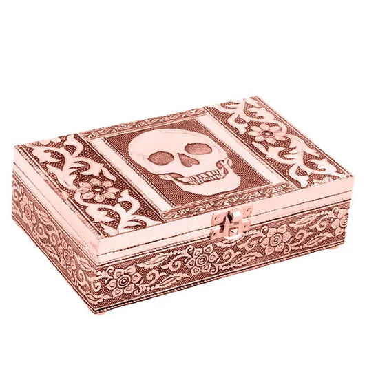 A rectangular decorative box with a skull motif on the lid, featuring ornate floral scrollwork patterns in a metallic rose gold finish, set against a plain white background.