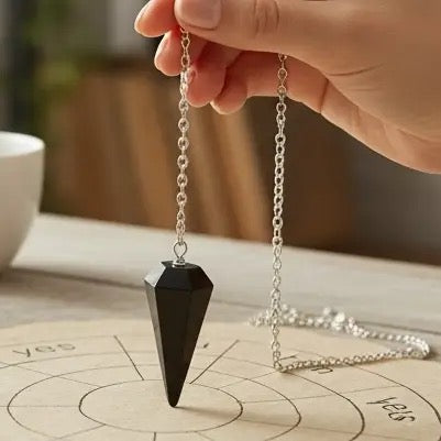 Black pendulum on a chain held by a hand over a divination board with 'yes' and 'no' circles.