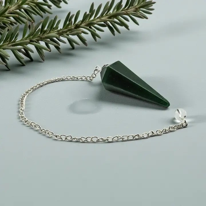 Green crystal pendulum on a silver chain with a green leafy branch on a light gray background