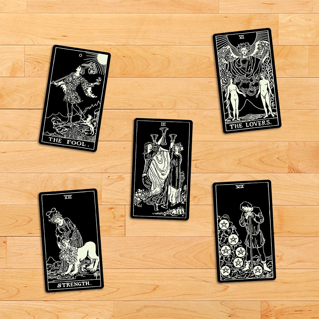 Five tarot cards from different decks arranged on a wooden surface.