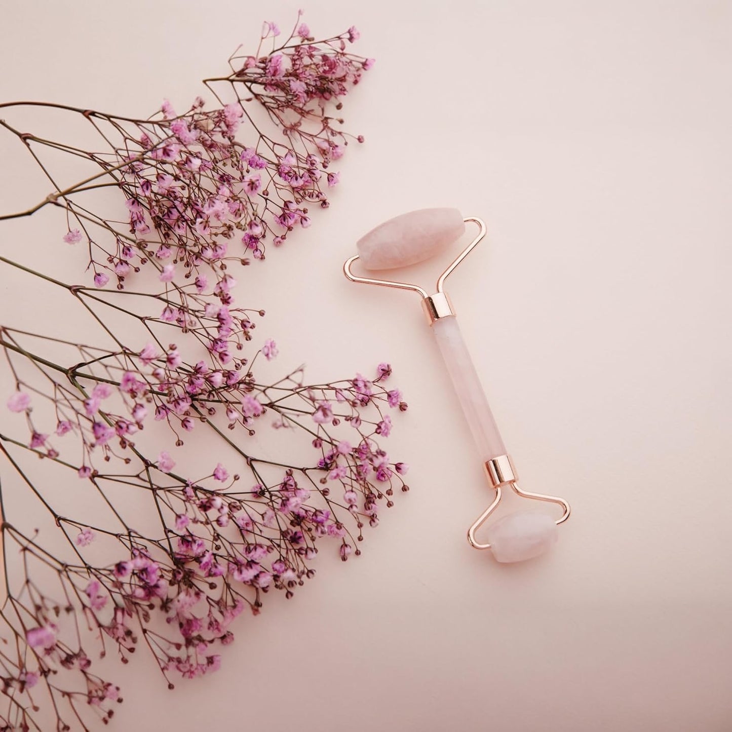 Rose Quartz massage roller with pink flowers and background.