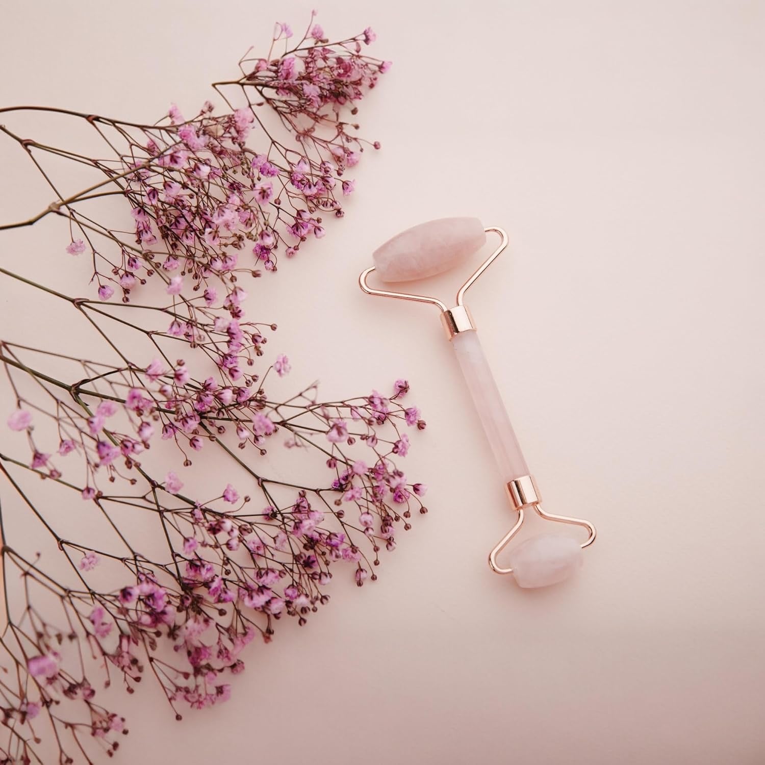 Rose Quartz massage roller with pink flowers and background.