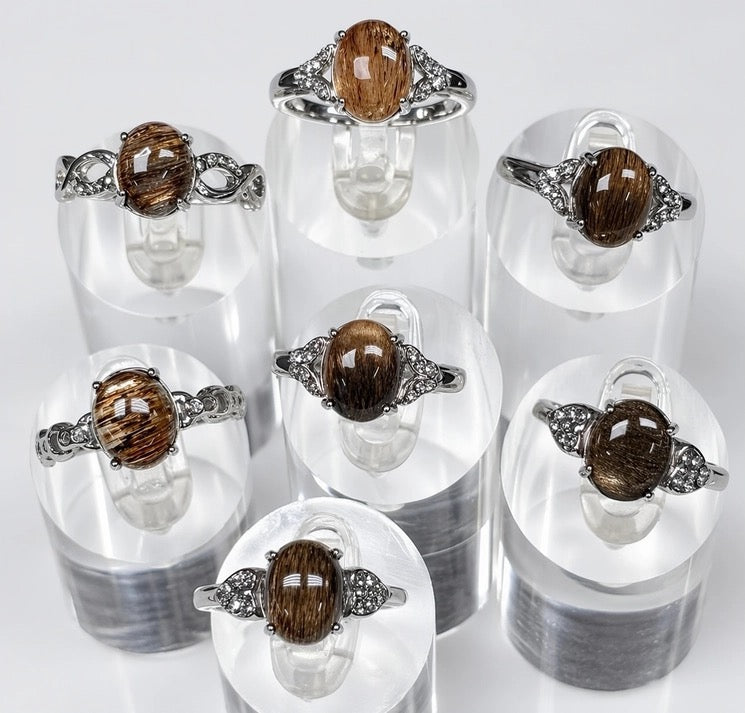 Set of rings with brown gemstones on clear stands against a white background