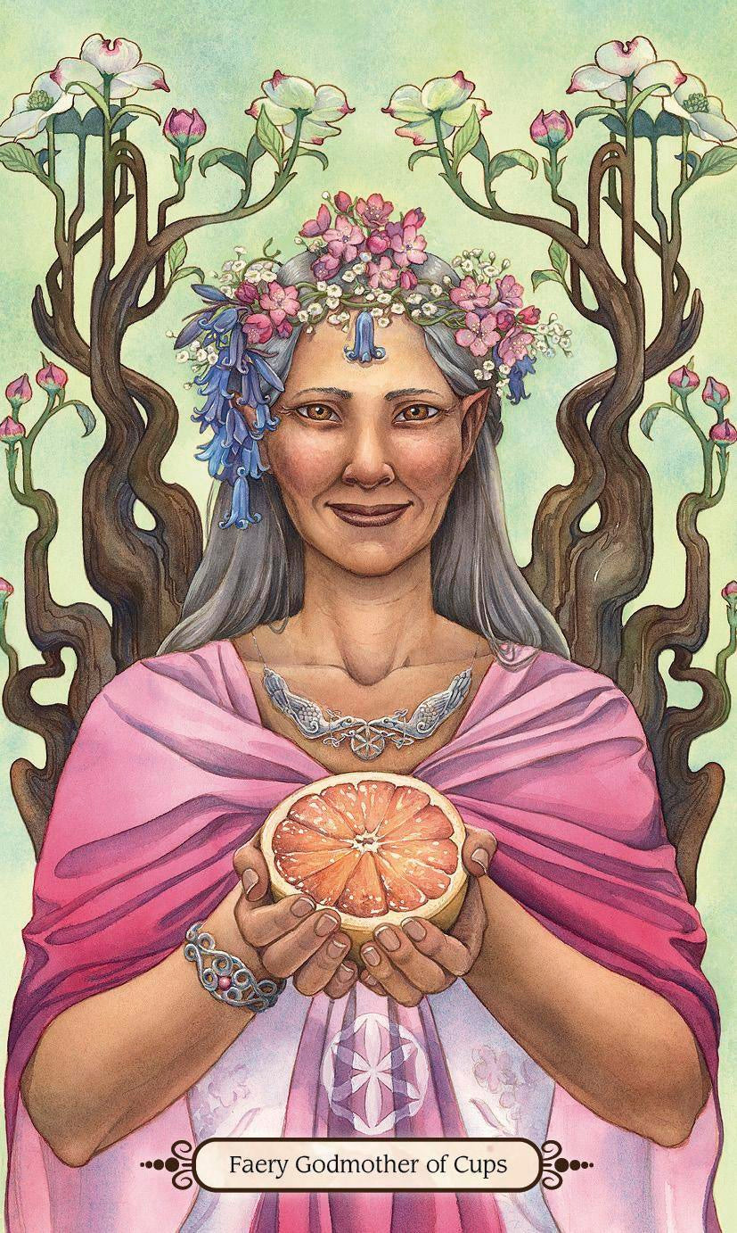 A stylized illustrated card or print showing a woman with gray hair, a floral crown, and pink draped robes holding a sliced grapefruit. Twisted tree branches with flowers frame her, and the text 'Faery Godmother of Cups' appears at the bottom.