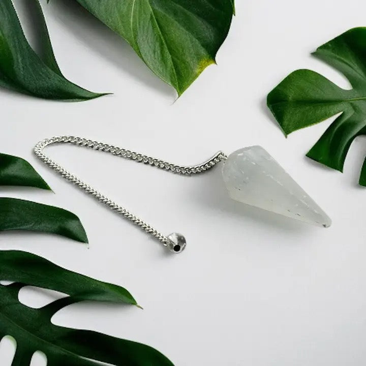 Crystal pendulum on a white surface with green leaves