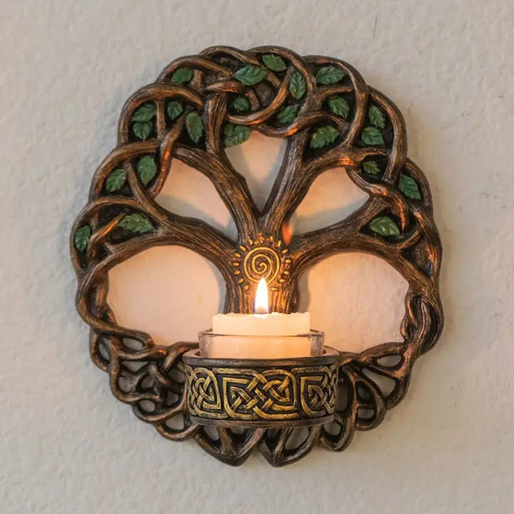 Decorative wall sconce with tree of life design holding a lit candle against a neutral background