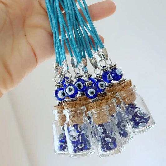 Small glass jars with cork lids containing blue evil eye charms on turquoise strings, held by a hand.
