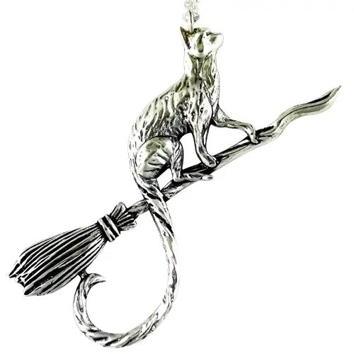 A silver-toned metal pendant featuring a detailed cat perched on a broomstick, shown against a plain white background.