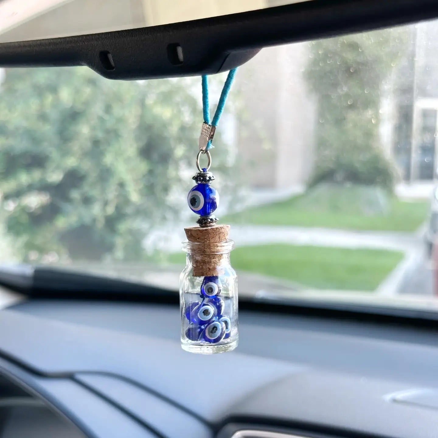 Car dashboard with a decorative charm featuring blue evil eye beads in a glass bottle.