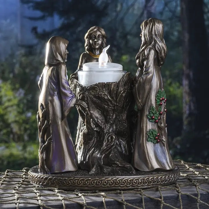 Decorative statue with three figures around a candle on a textured surface with a blurred natural background