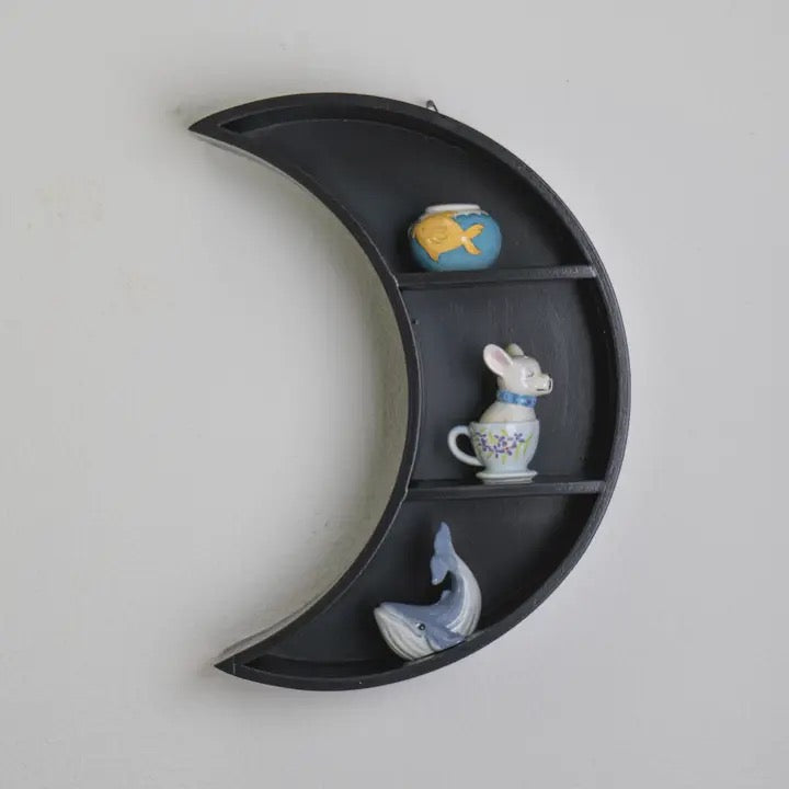Crescent moon-shaped wall shelf with decorative items on a plain background