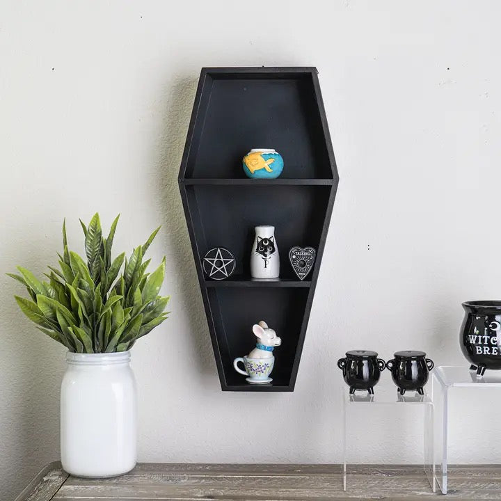 Black coffin-shaped shelf with decorative items against a white wall.