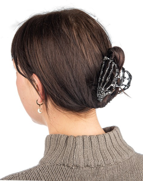 Person with dark hair styled in a bun using a decorative hair clip on a white background