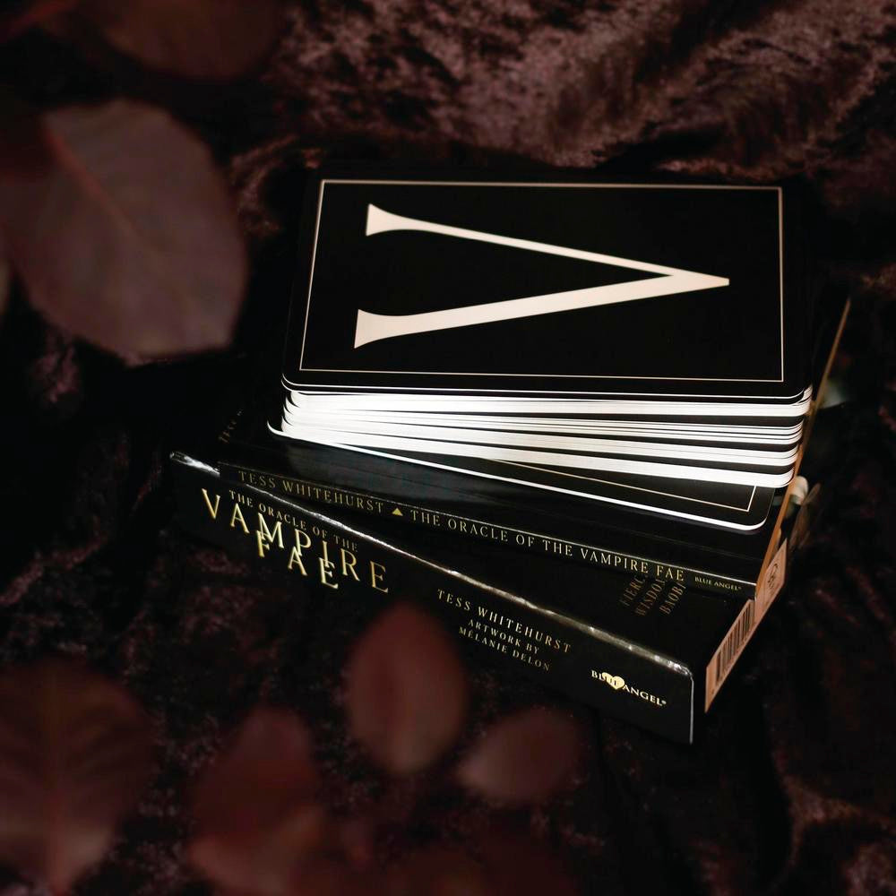 Stack of books titled 'The Oracle of the Vampire Fae' with a card featuring a white triangle symbol on a dark background.