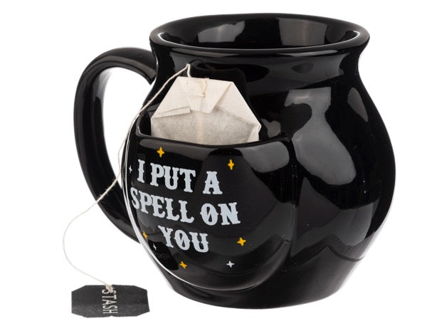 Black mug with 'I Put a Spell on You' text and tea bag inside, on a white background