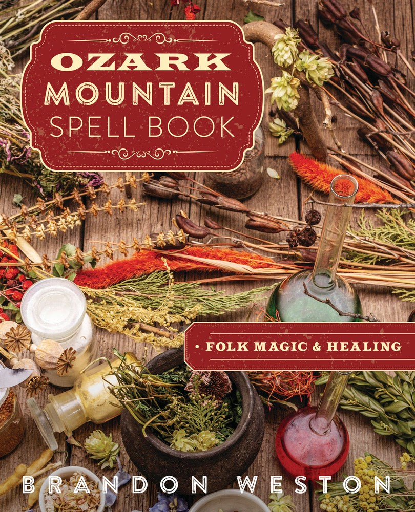 Book cover of 'Ozark Mountain Spell Book' with herbs and magical items on a wooden background