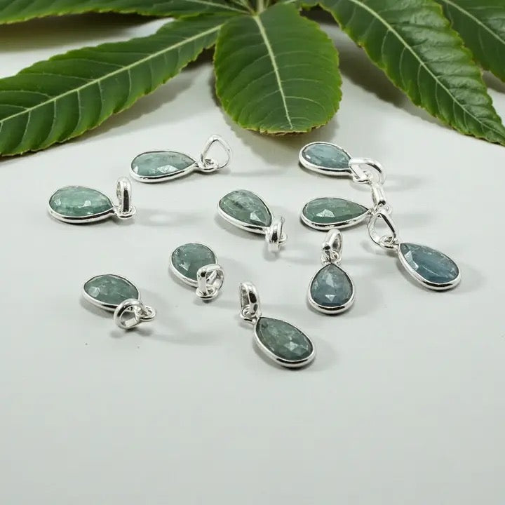 Teardrop-shaped green gemstone pendants on a white surface with green leaves in the background