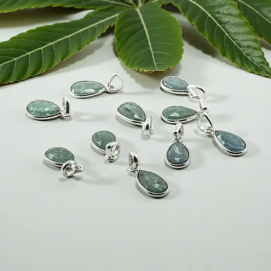 Teardrop-shaped green gemstone pendants on a white surface with green leaves in the background