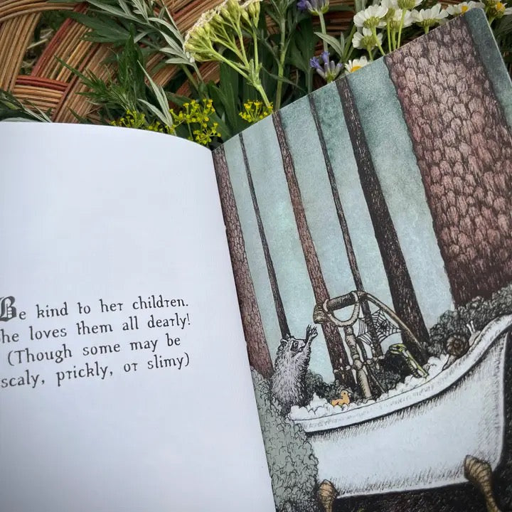 An open children's book spread showing a printed page with text on the left and an illustrated scene of a small animal in a bathtub on the right. The book is photographed outdoors with flowers and woven mat visible around it.