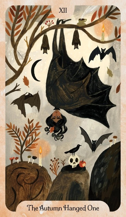 A tarot-style illustrated card titled 'The Autumn Hanged One' with the Roman numeral XII at the top. The artwork shows hanging bats, a small owl, a skull on a rock, autumn leaves, candles, and a dark bird against a muted beige and brown background.