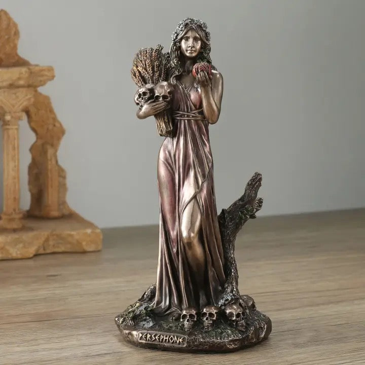 Statue of a woman in a flowing dress holding a skull and a fruit on a wooden surface.