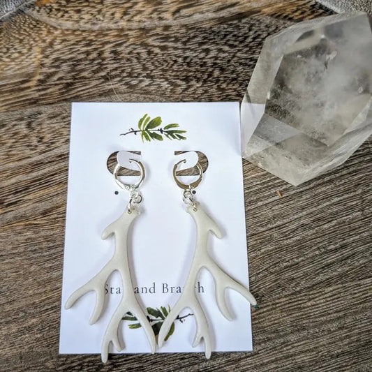 White antler-shaped earrings on a card with 'Star and Branch' branding, placed on a wooden surface.