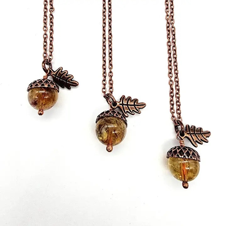 Three acorn-shaped necklaces with leaf charms on a white background