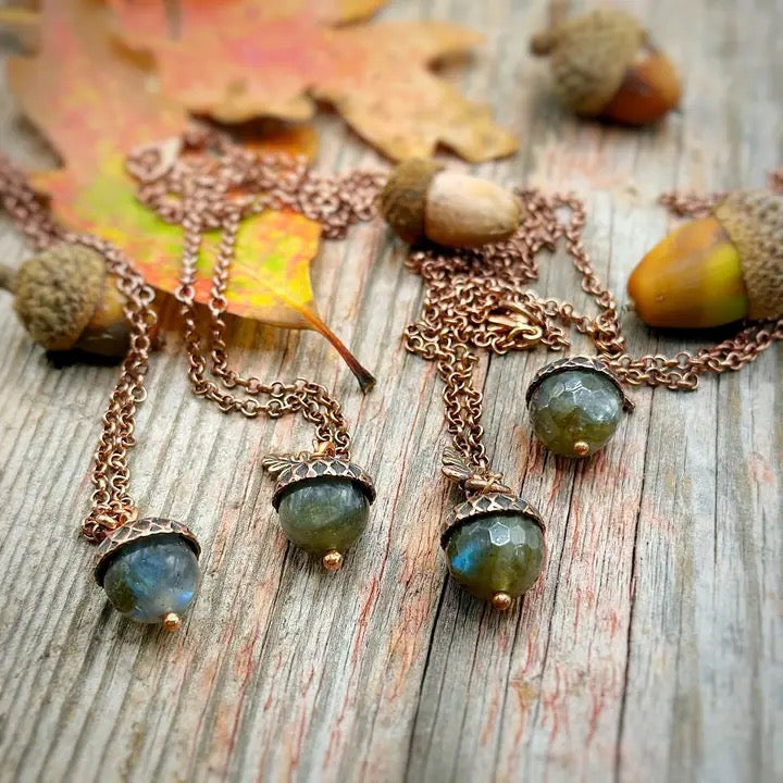 Three labradorite necklaces on a wooden surface with acorns and leaves.