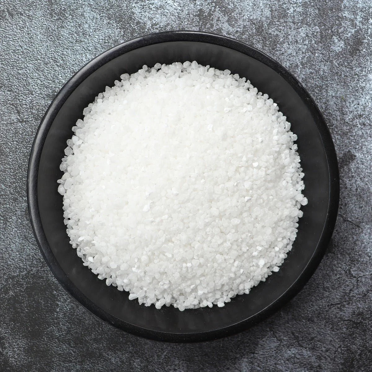 White granulated product in a black bowl on a gray surface