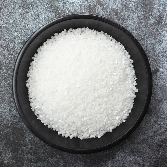 White granulated product in a black bowl on a gray surface