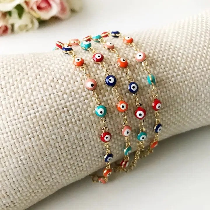 Colorful evil eye beaded necklaces on a textured surface with flowers in the background