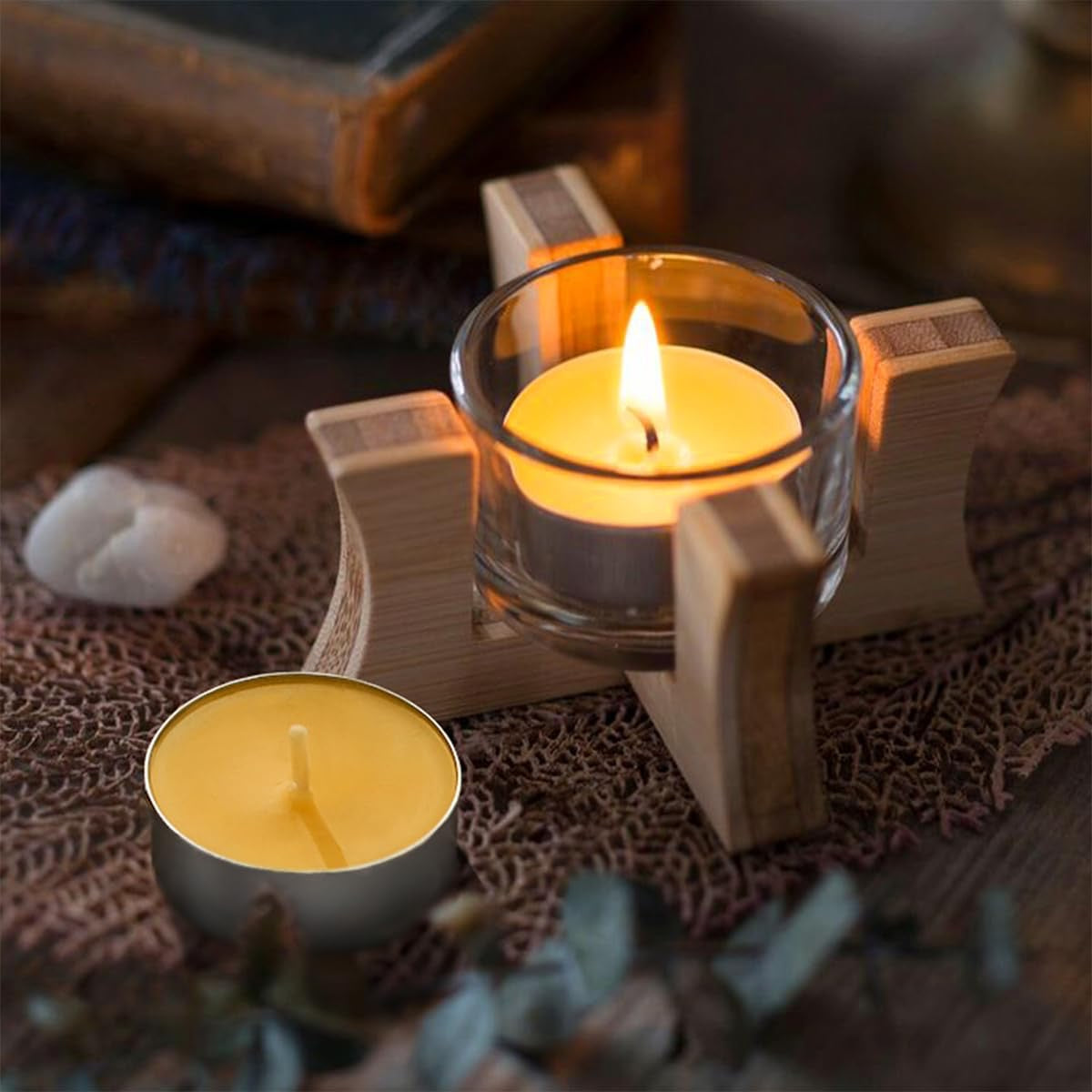 One candle in a glass holders one unlit on a textured surface with a blurred background