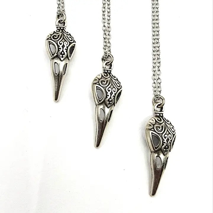 Three silver bird skull pendants on chains against a white background