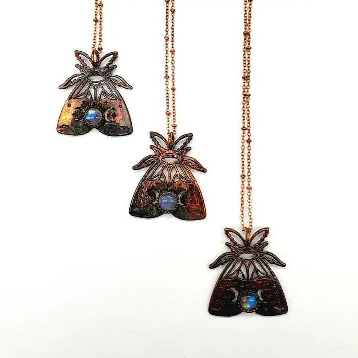 Three moth pendants on rose gold chains against a white background