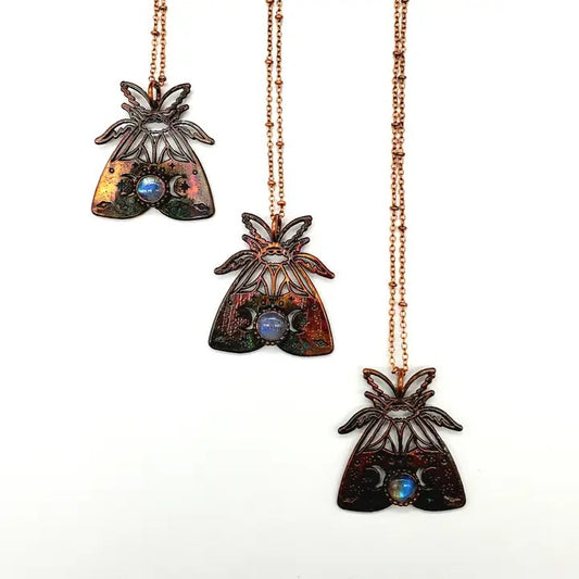 Three moth pendants on rose gold chains against a white background