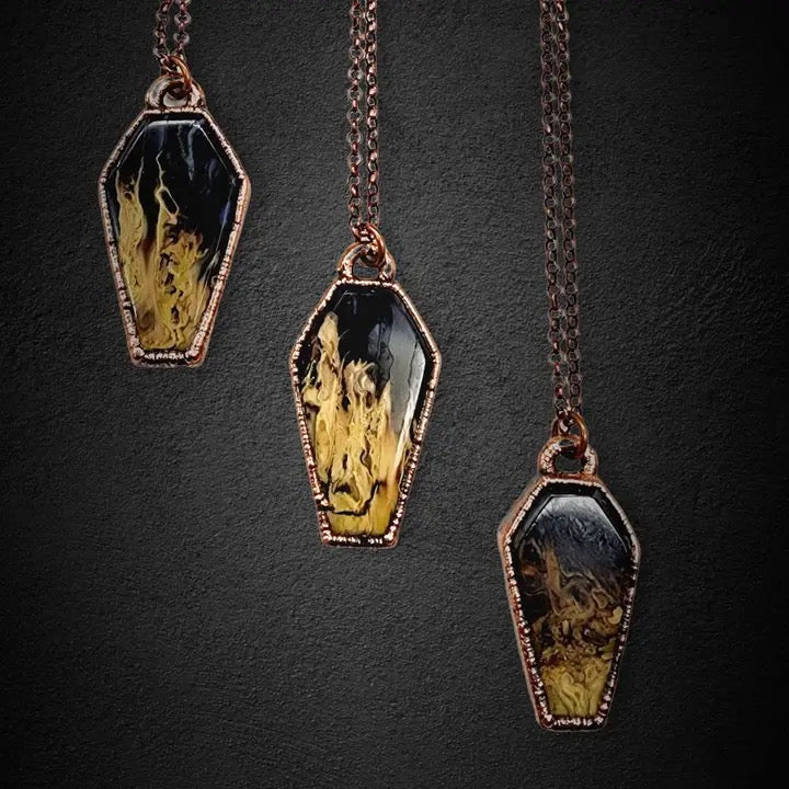 Three pendant necklaces with coffin-shaped pendants on a dark background