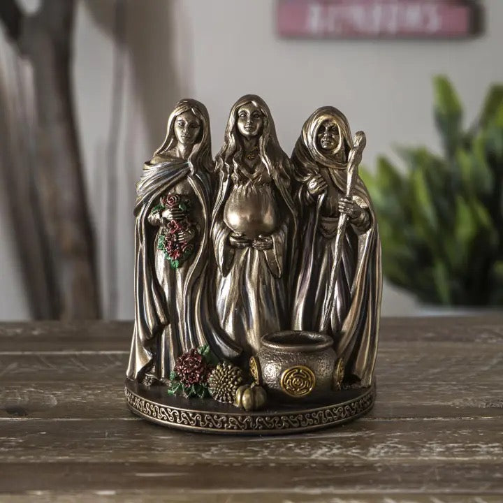 Bronze figurine of three women with a pot on a wooden surface