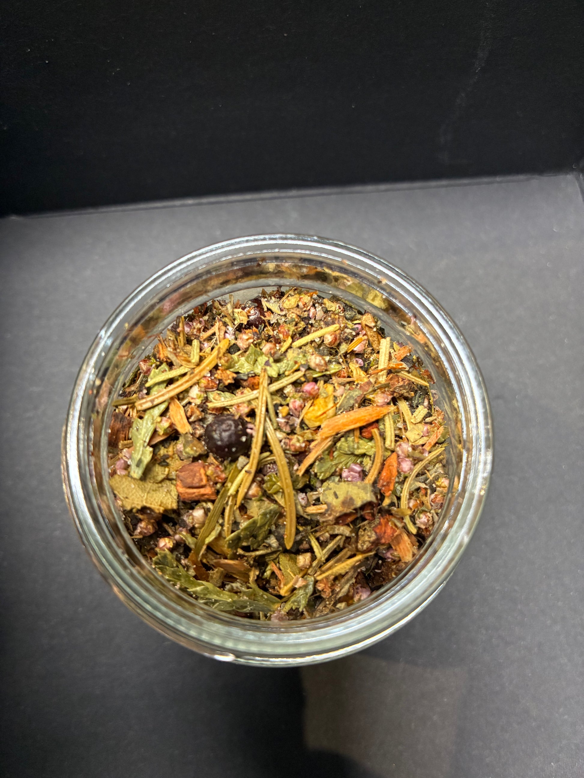 Glass jar filled with dried herbs and spices on a dark surface