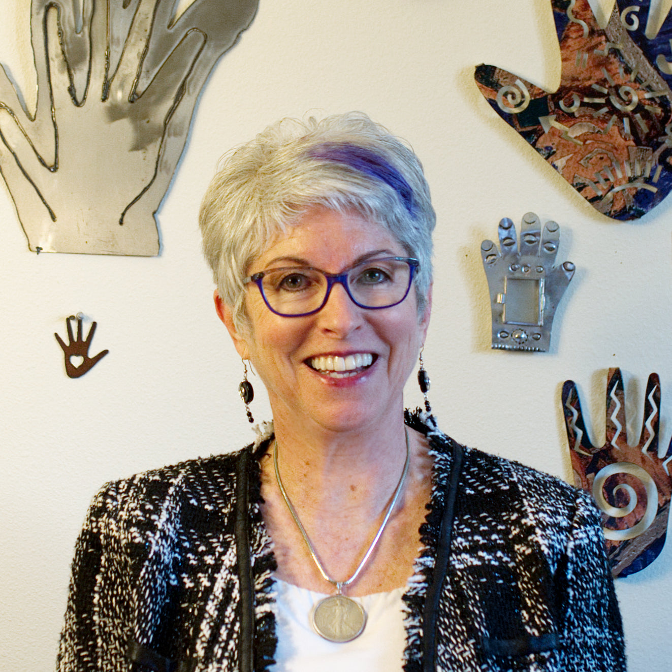 Woman with short gray hair and glasses standing in front of decorative wall art.