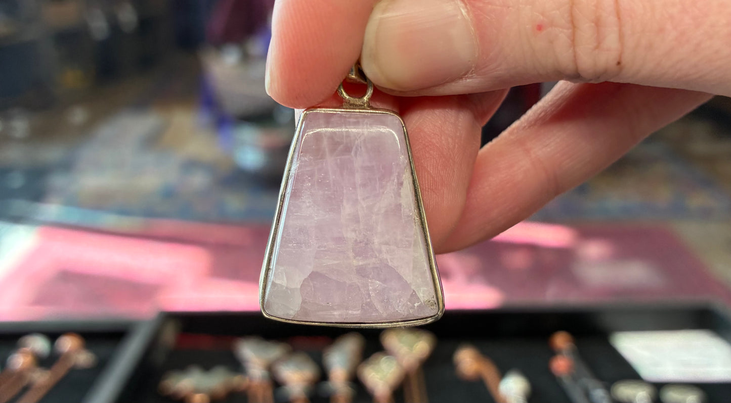 Hand holding a pink stone pendant with silver setting 