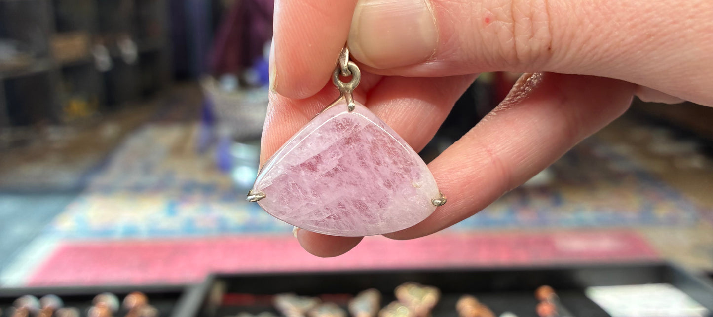 Hand holding a pink stone pendant with a blurred background