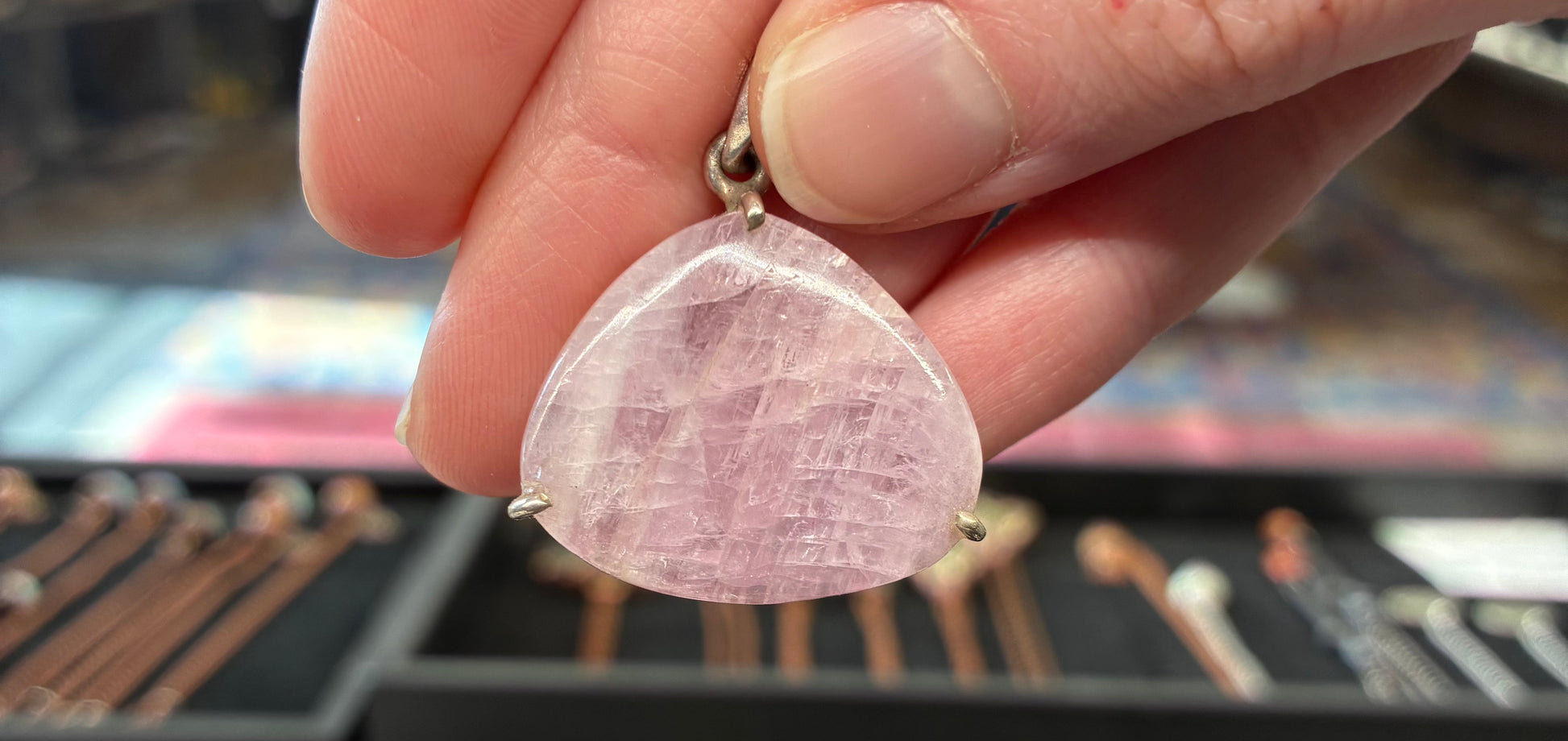 Hand holding a pink triangle-shaped stone pendant 