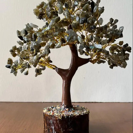 A labradorite crystal tree on gold-colored wire branches, mounted on a brown wooden trunk and a textured multicolor base.