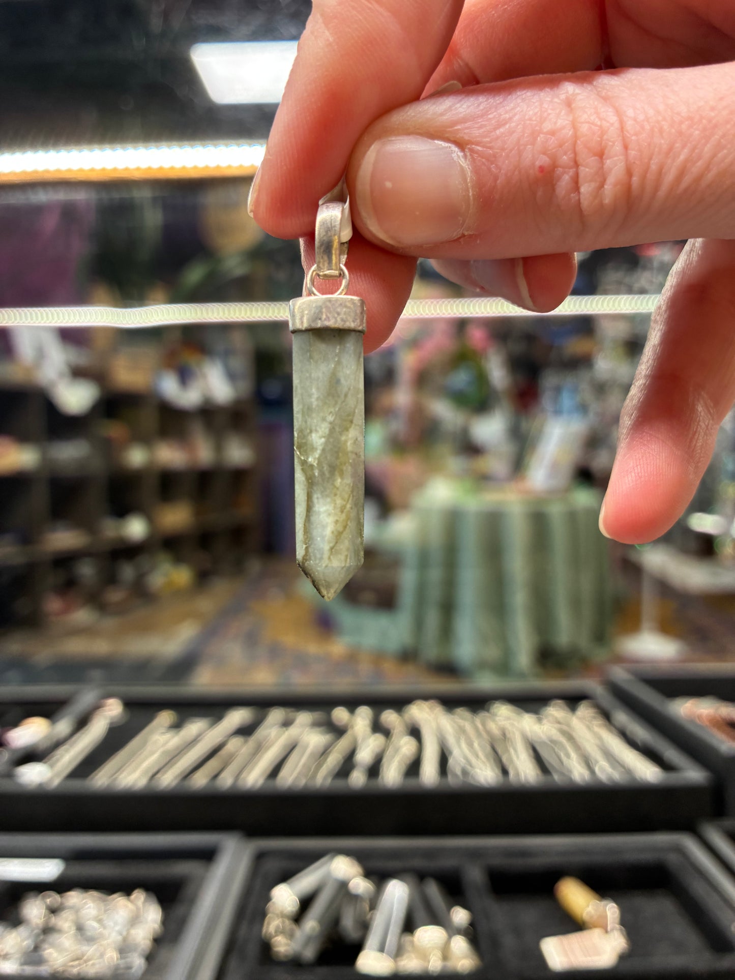 Hand holding a crystal pendant with a blurred store background