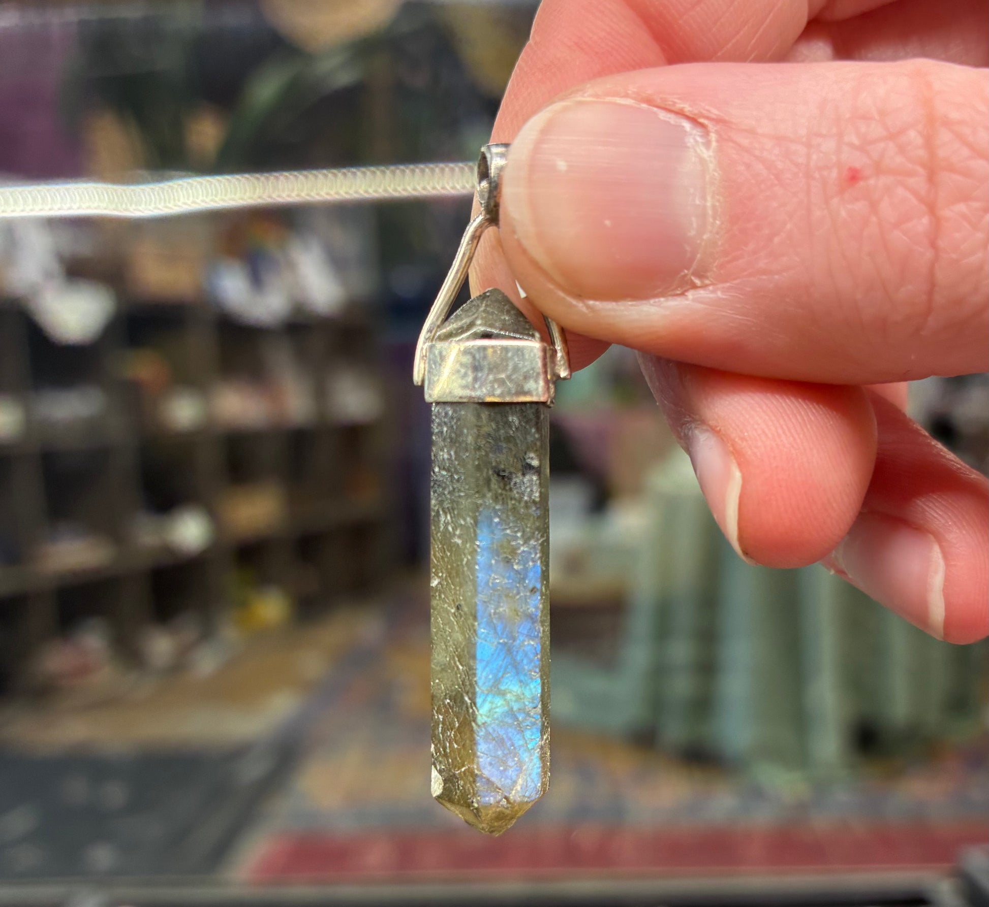 Hand holding a crystal pendant with a blurred store background