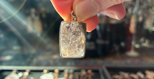 Hand holding a rectangular crystal pendant with a blurred background