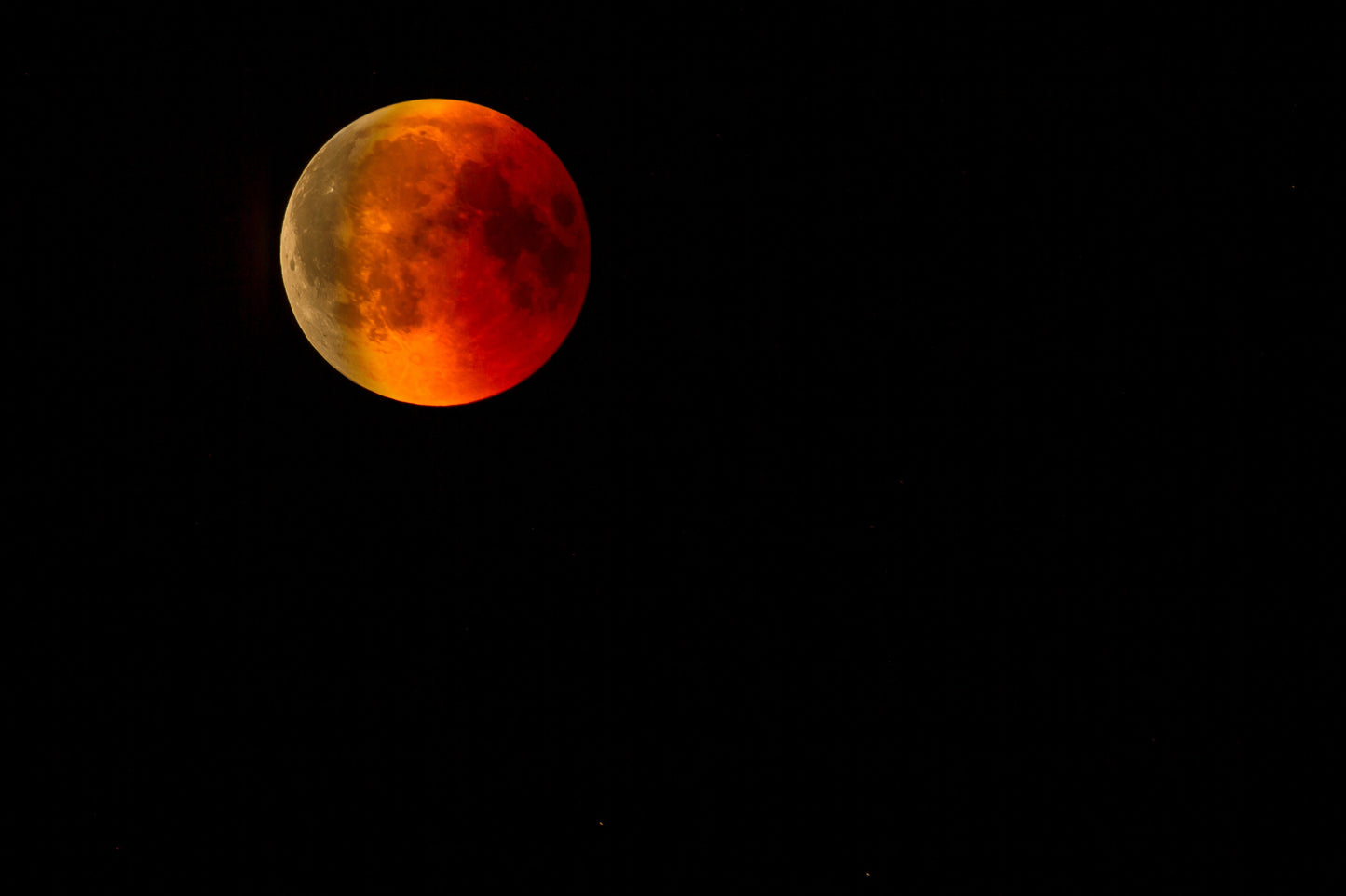 Partial lunar eclipse with a red-orange hue on a black background